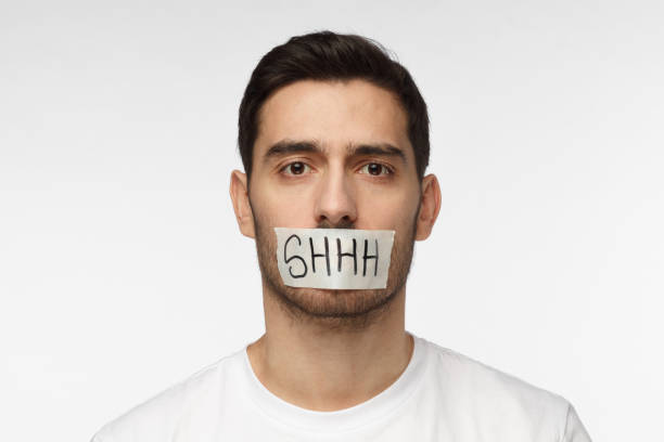 close-up-shot-of-young-man-with-taped-mouth-with-shhh-text-on-it-picture-id1015970764